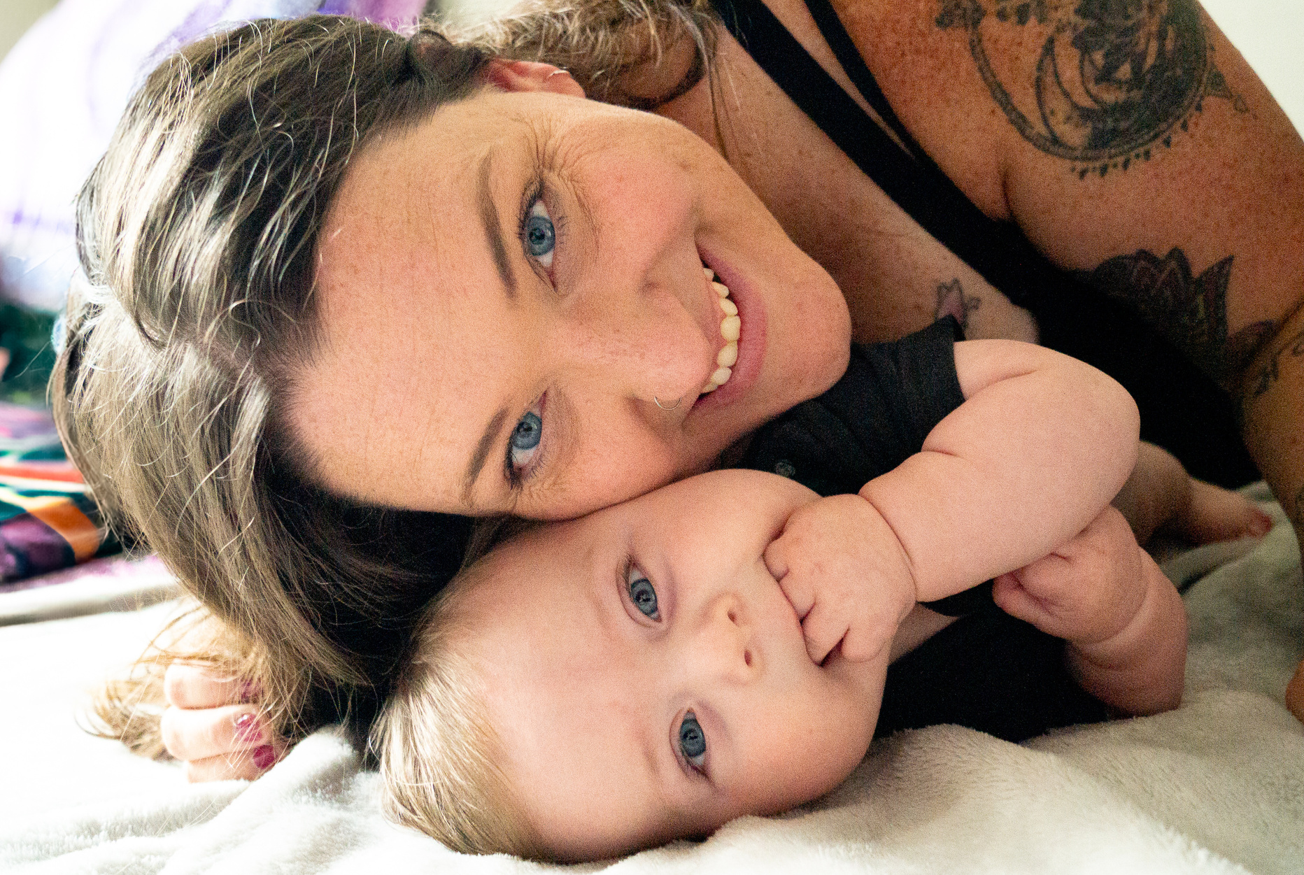 a person with tattoos and a baby laying on a bed