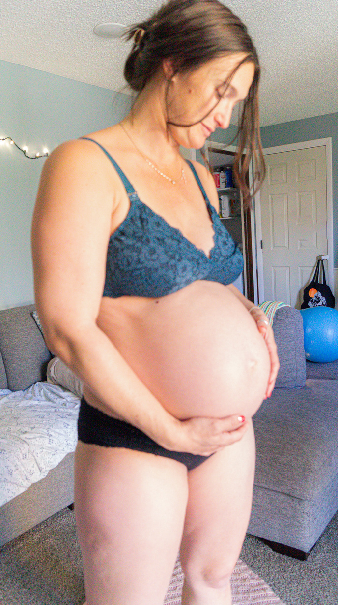 A pregnant woman standing in a living room with her hands on her belly