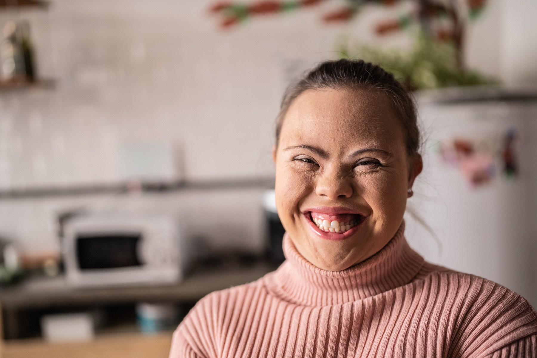 a person smiling in a pink sweater standing in front of a refrigerator