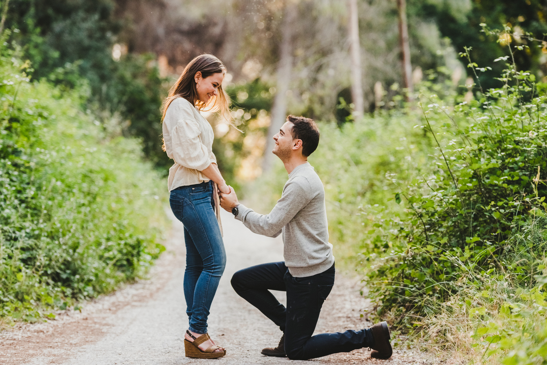 a person kneeling down to propose to their partner in the middle of a forest