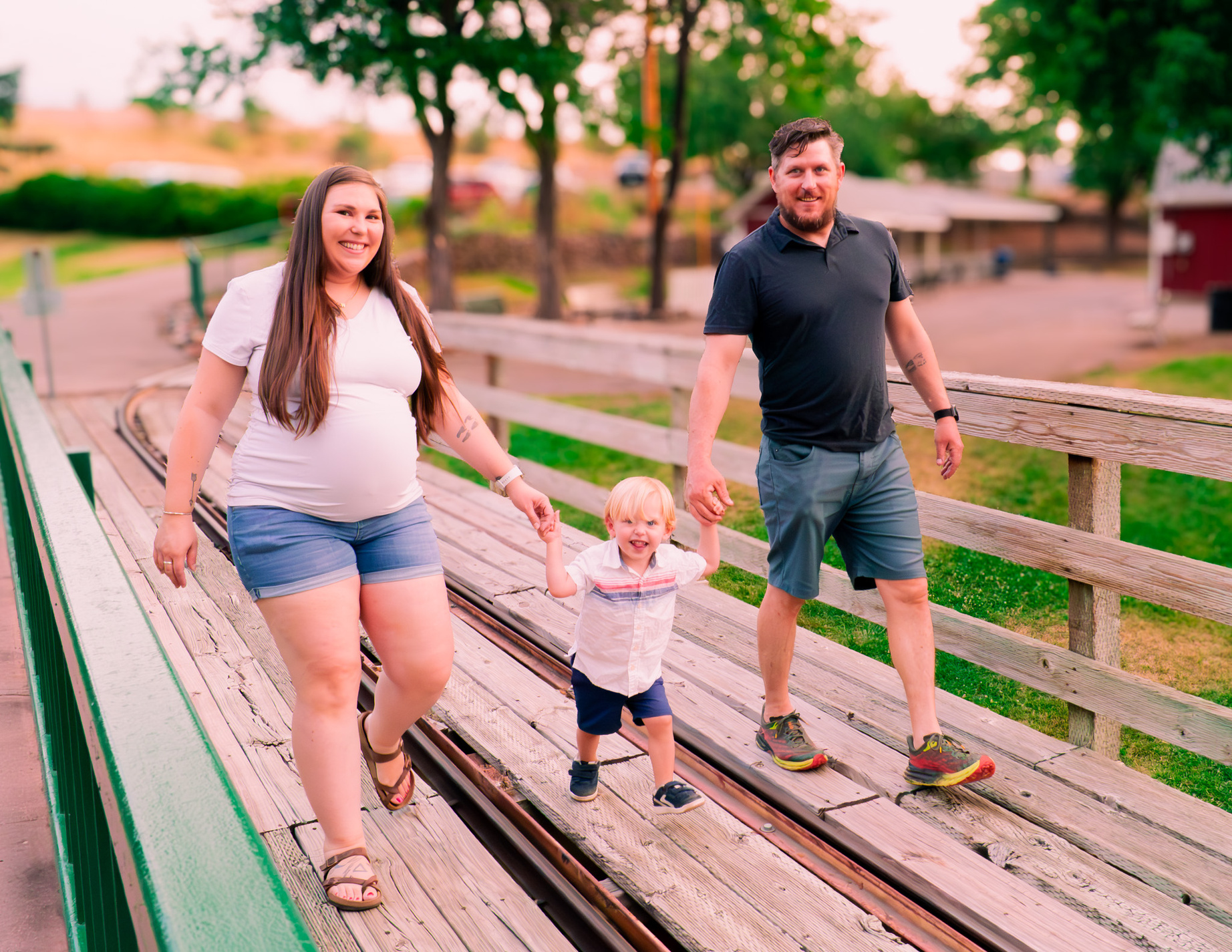 a pregnant person, person and child walking on a wooden bridge