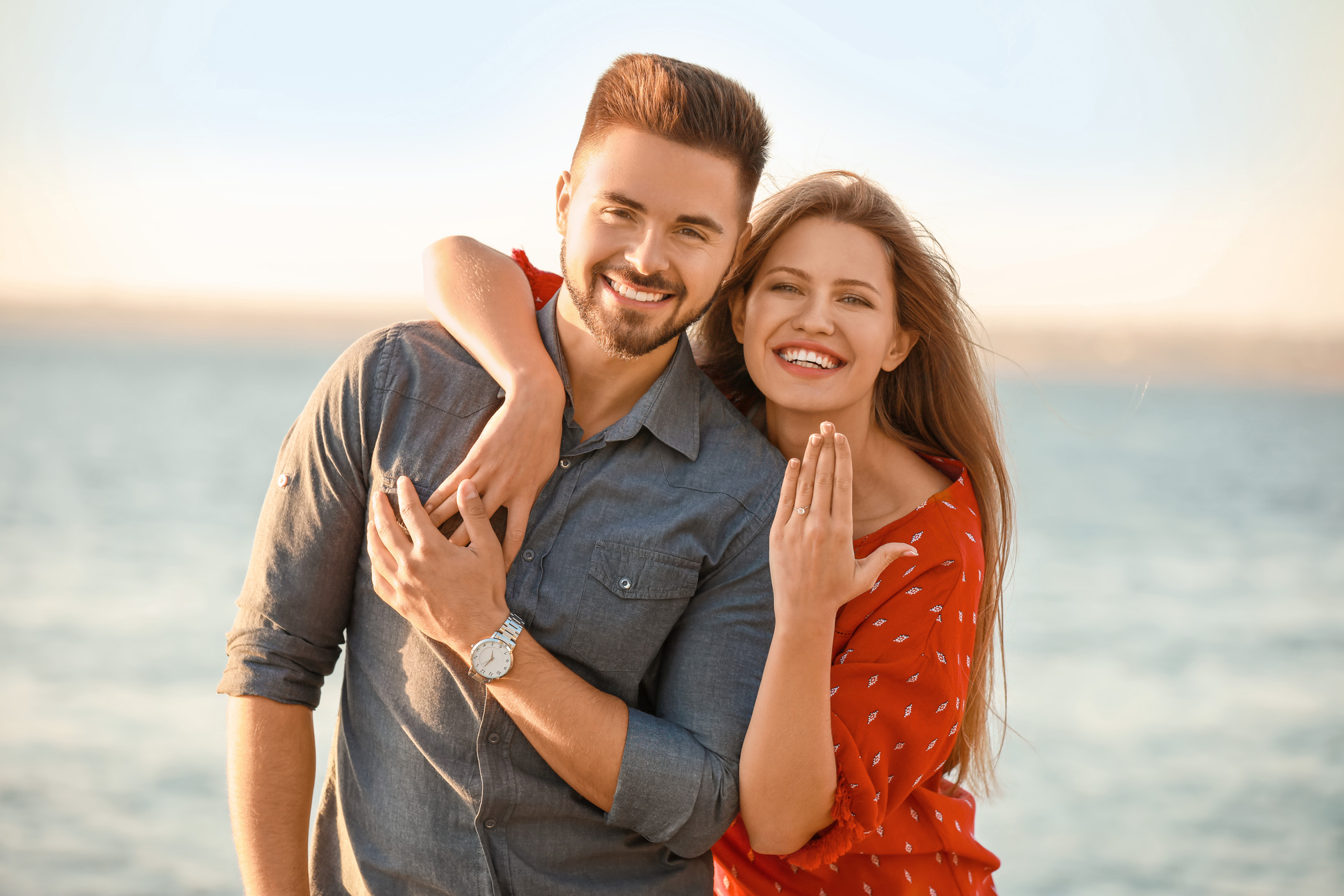 Two people hugging on the beach with the ocean in the background.