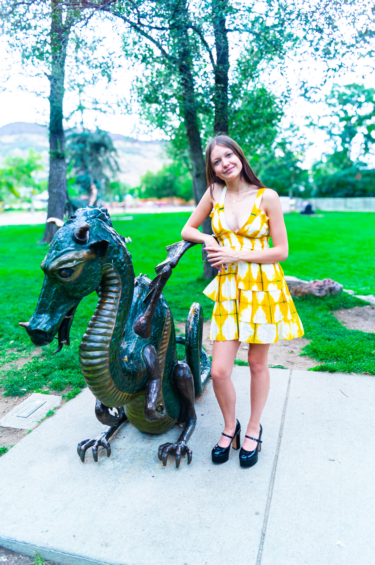 a person in a yellow dress standing next to a statue of a dragon