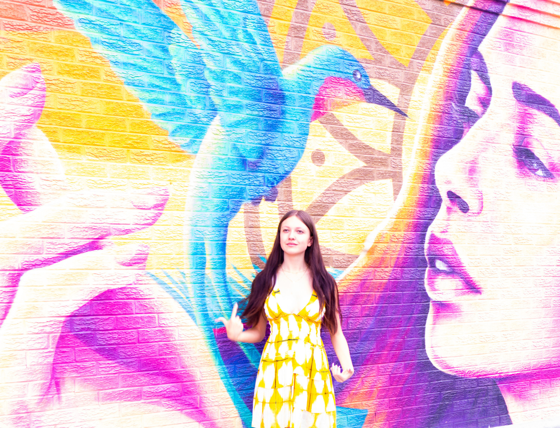 A person in a yellow dress standing in front of a colorful wall