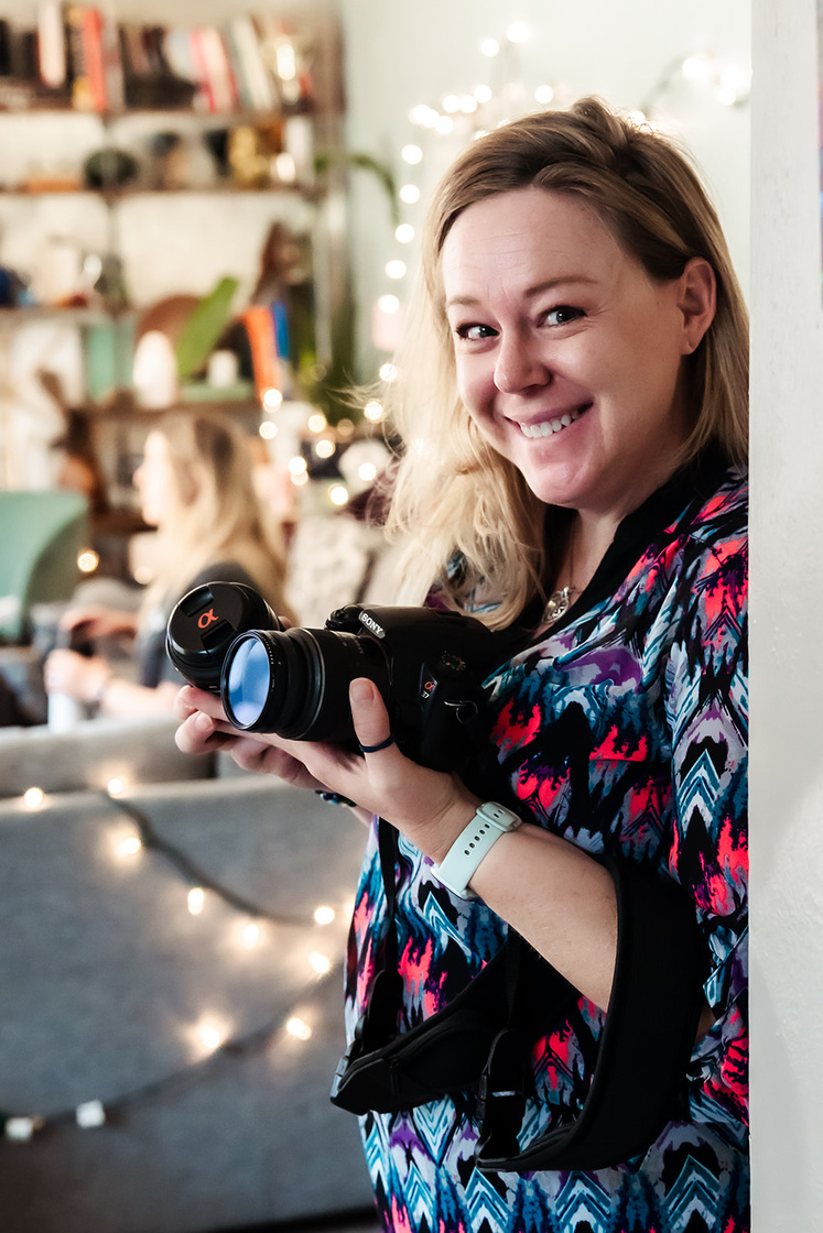 a smiling person holding a camera in front of a christmas tree